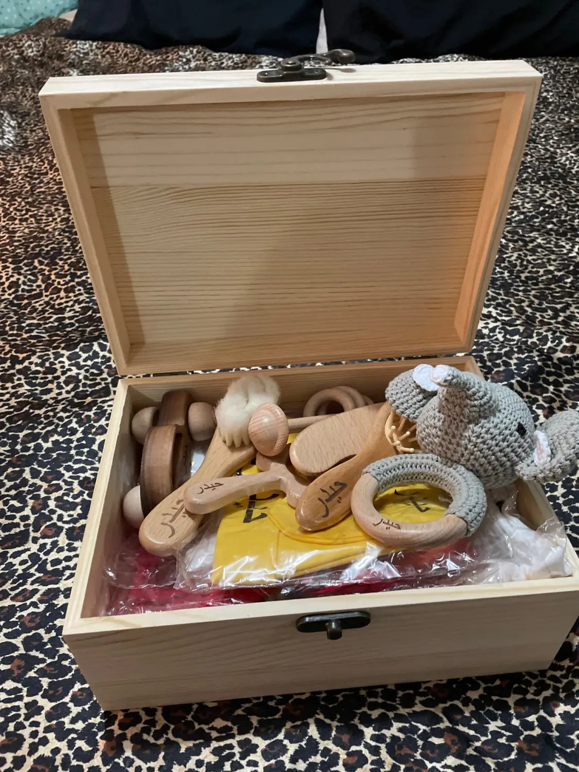 淡色の木製ベビートイ一式が、同系統のナチュラルウッドの収納箱に収まった状態で入った、パーソナライズされた木製の洗礼記念品保管箱。