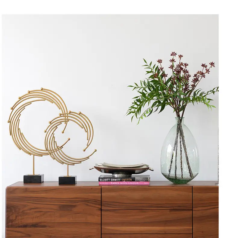 Gold-toned metal abstract sculpture featuring interlocking circular rings on black square bases designed as office desk decor.