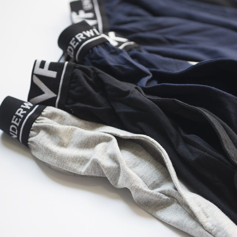 A stack of men cotton boxer shorts in gray black and navy blue with elastic waistbands featuring white lettering designed for loose casual lounge gym and jogging use.