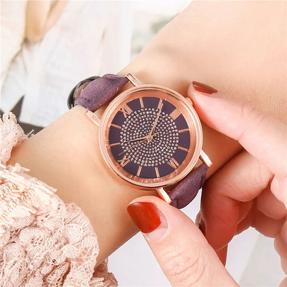 Rose gold crystal quartz women watch with a dark purple rhinestone-adorned dial, roman numerals, and a matching rose gold-toned suede leather strap.