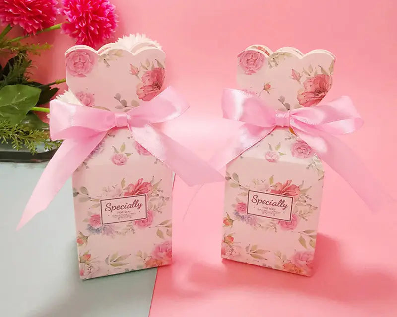 Rosa blumig gemusterte Hochzeits-Gastgeschenkboxen mit gewellten Oberkanten und passenden Satinbändern, entworfen für eine elegante Geschenkpräsentation.