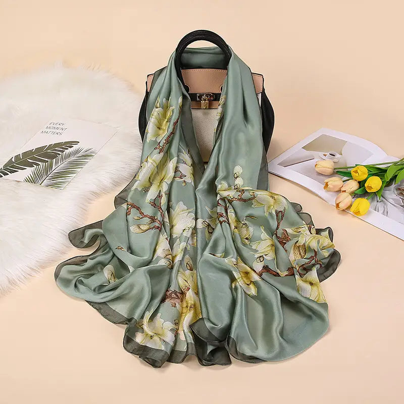 Un châle foulard en soie vert sauge fluide, orné d’un délicat motif floral de fleurs blanches et jaunes sur des branches brun foncé, inspiré par les amandiers en fleurs de Van Gogh