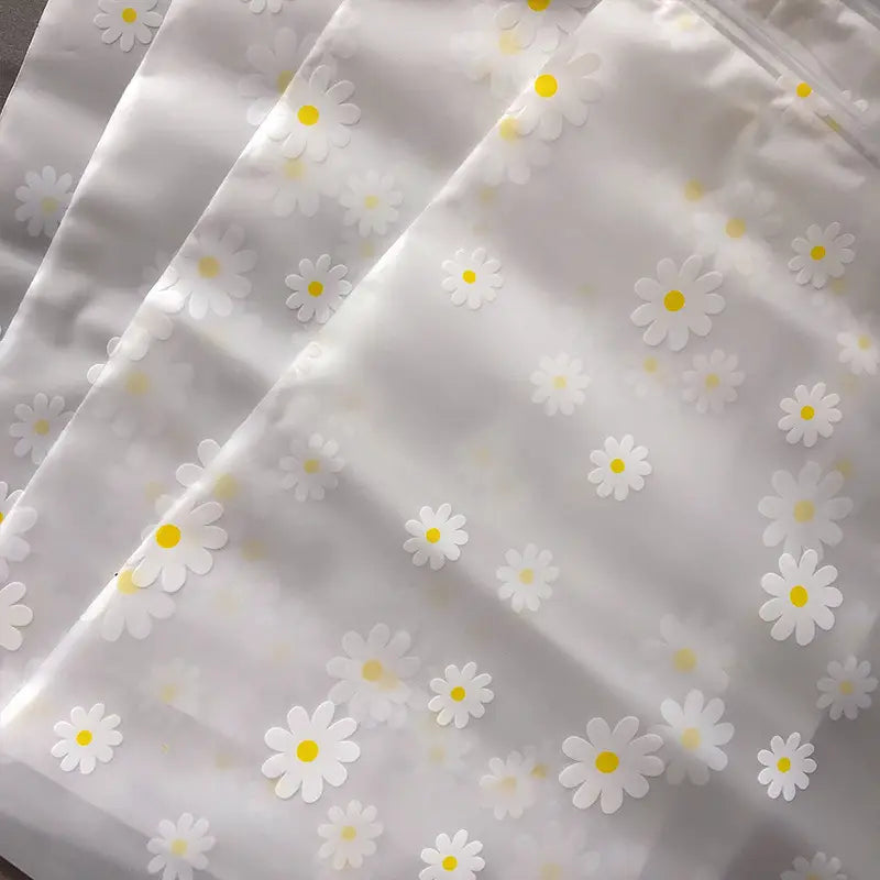 Blumige, durchsichtige Reisekosmetiktasche aus transparentem Kunststoff mit einem zarten Muster aus weißen Gänseblümchen mit gelben Zentren.