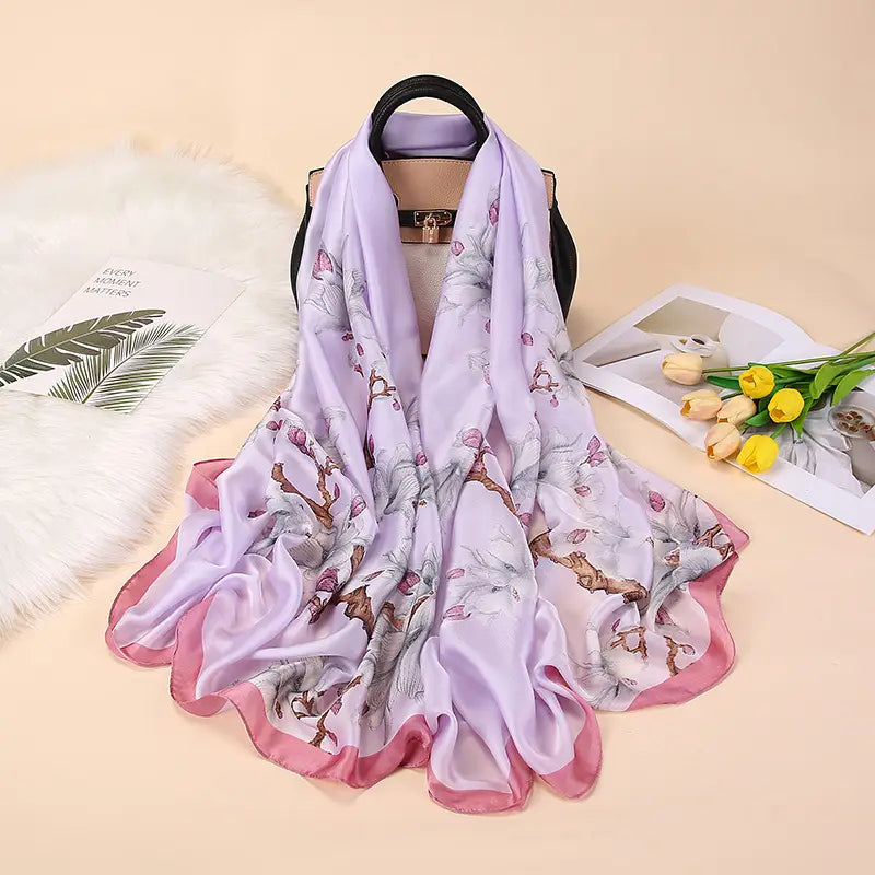 Un foulard en soie lilas délicat, avec un ourlet rose doux, arborant un motif floral élégant de fleurs sur des branches, issu de la collection de châles foulards en soie « Van Gogh Almond Blossom ».
