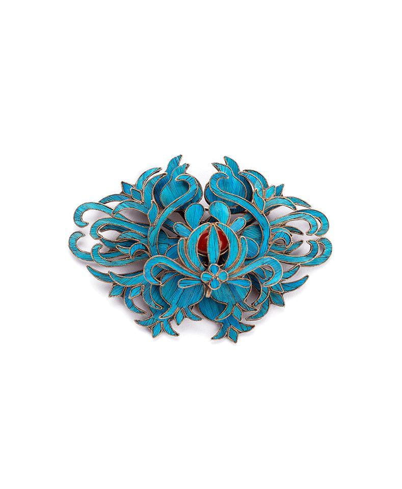 A filigree brooch featuring vibrant turquoise enamel with intricate floral and leaf patterns accented by a central red gemstone in palace jewelry style.