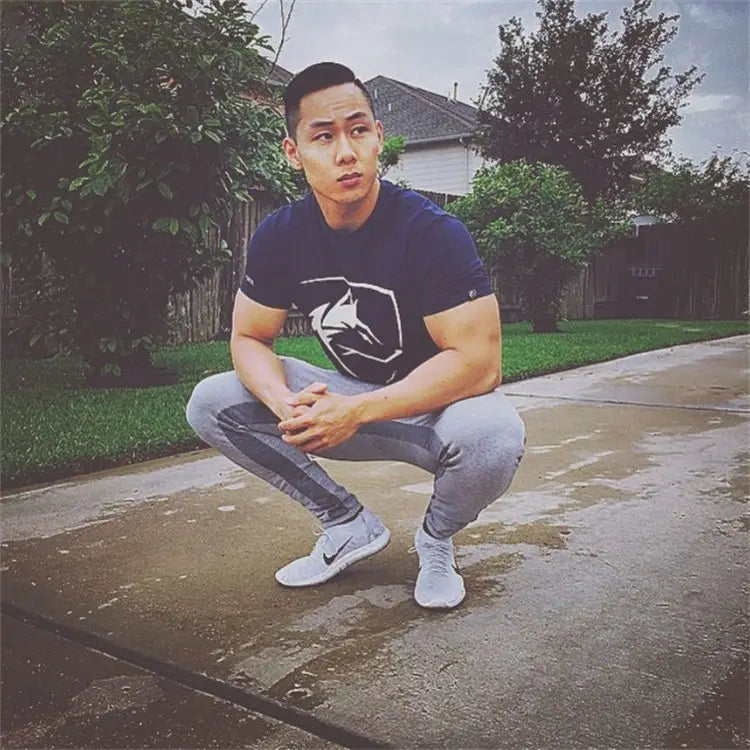 Homme portant un t-shirt d’entraînement gothique pour homme en coton bleu marine, avec logo de loup gothique, associé à un pantalon de survêtement gris.