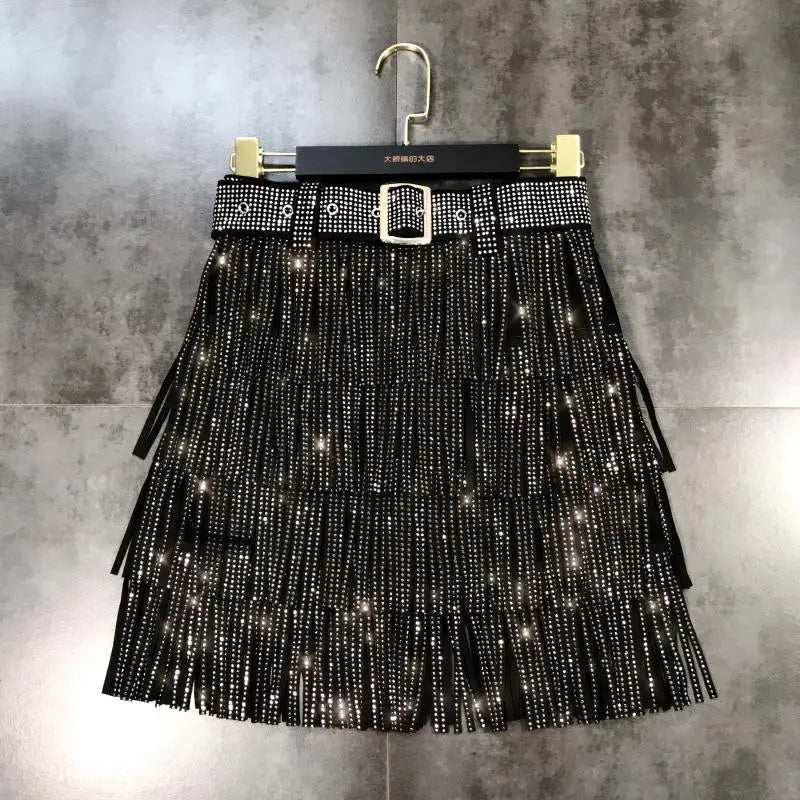 mini-jupe noire à franges agrémentée de strass scintillants et d’une ceinture assortie à rivets, avec boucle argentée, issue de la collection de mini-jupes taille haute à franges en strass