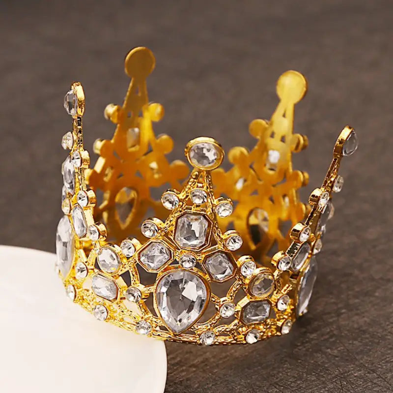 Ein goldener, kunstvoller Mini-Kronen-Tortenaufsatz und eine Haar-Tiara, verziert mit klaren facettierten Kristallen und aufwendiger Metallverarbeitung.