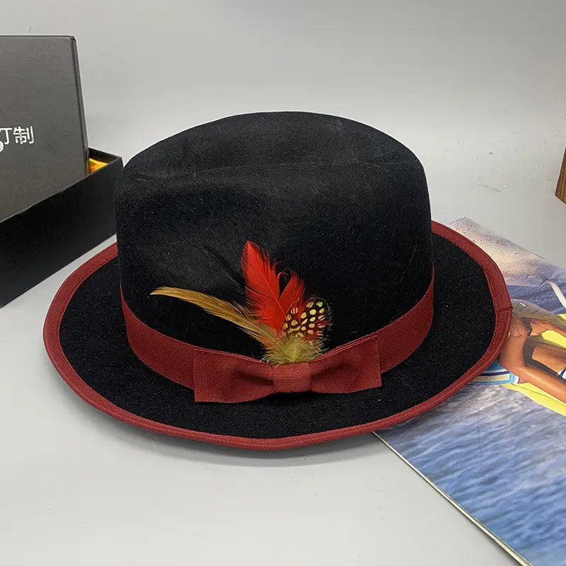 A black woolen felt fedora hat with a red ribbon bow and decorative feather accent unisex design.