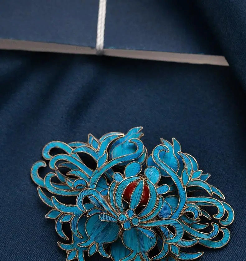 A vibrant turquoise enamel filigree brooch with intricate floral design and a central red gemstone accent for elegant palace jewelry.