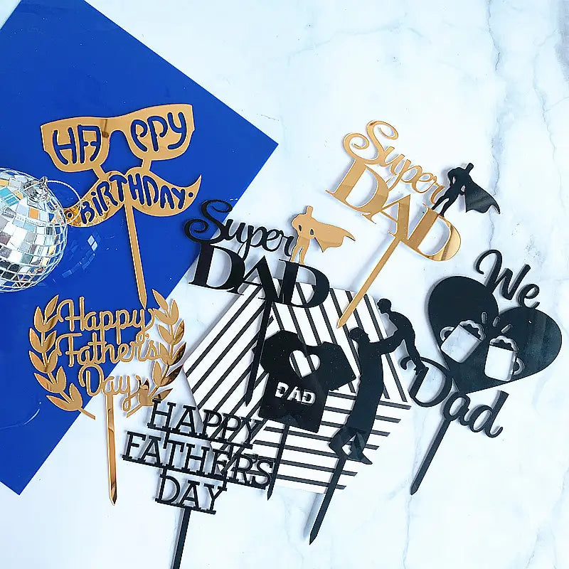 Gold and black metallic acrylic cake toppers featuring Father’s Day designs including super dad text, a superhero silhouette, and coffee mugs.