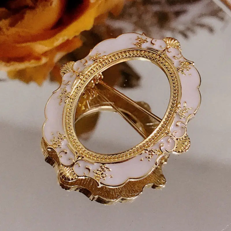 Broche para marco de cuadro con arte de David barroco, con una pinza para el cabello ornamentada delicada en rosa y oro, con centro espejado y grabados florales intrincados a lo largo de los bordes festoneados.