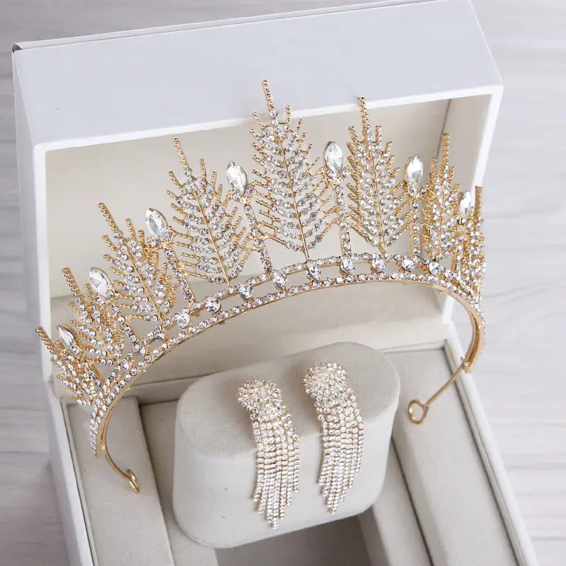 A gold-toned crystal bridal tiara and wedding crown headpiece with intricate leaf designs and clear crystals displayed in a white gift box with matching dangling earrings.