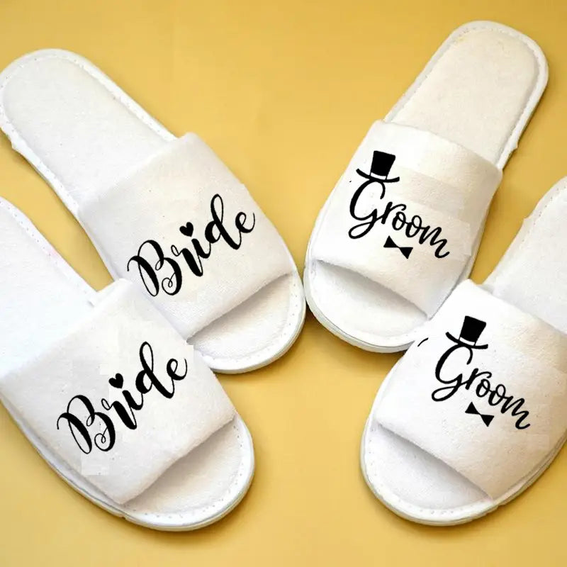 Weiße durchgehende Schlupf-Brautparty-Slipper mit einem auf der Vorderseite in schwarzer, geschwungener Handschrift gedruckten Motiv von Braut und Bräutigam, jeweils verziert mit einer Zylinderhut- und Fliege-Grafik für Hochzeits-Slipper.