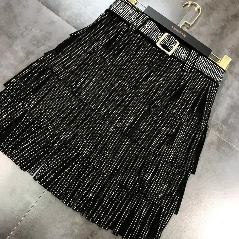 Mini-jupe noire à franges taille haute, agrémentée de strass scintillants et d’une ceinture assortie à rivets, avec boucle à tonalité dorée.