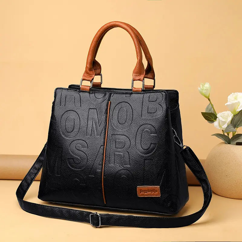 Black crossbody handbag style1 style2 made of black pu leather featuring tan handles and shoulder strap with embossed lettering across the front.