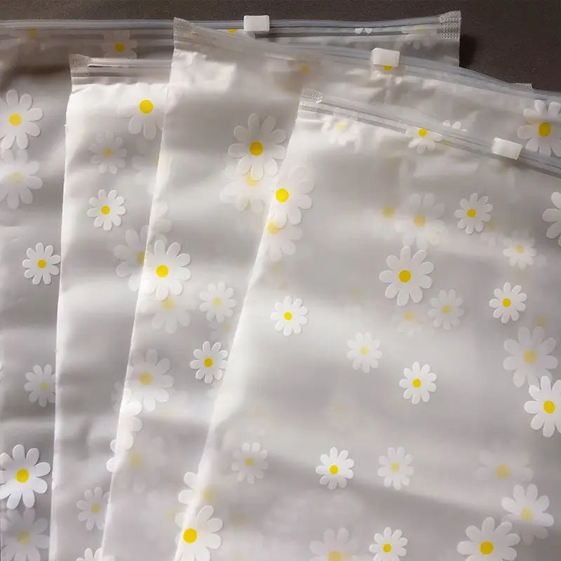 Blumige, durchsichtige Reisekosmetiktasche aus durchsichtigem Kunststoff mit einem zarten Muster aus weißen Gänseblümchen mit gelben Zentren und einer Reißverschlussöffnung.