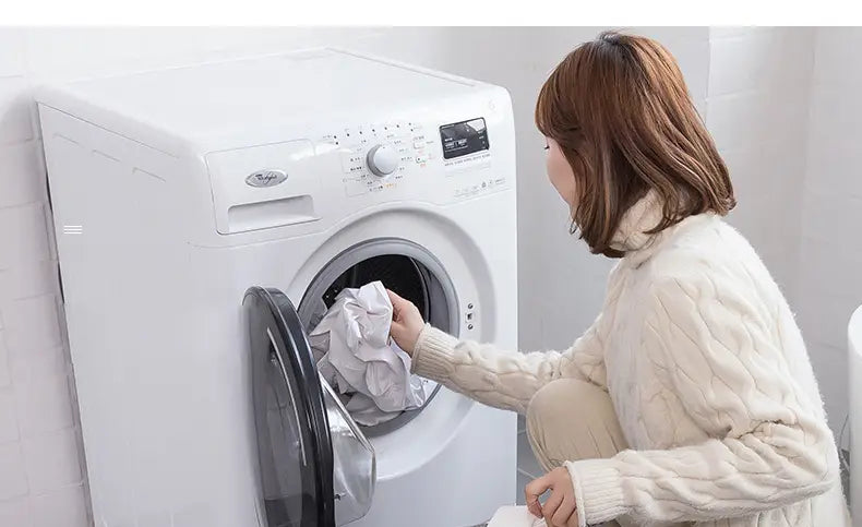 white front-loading washing machine with digital display and control panel placed next to a foldable laundry basket fabric storage box in beige color for organizing laundry baskets and foldable storage baskets.