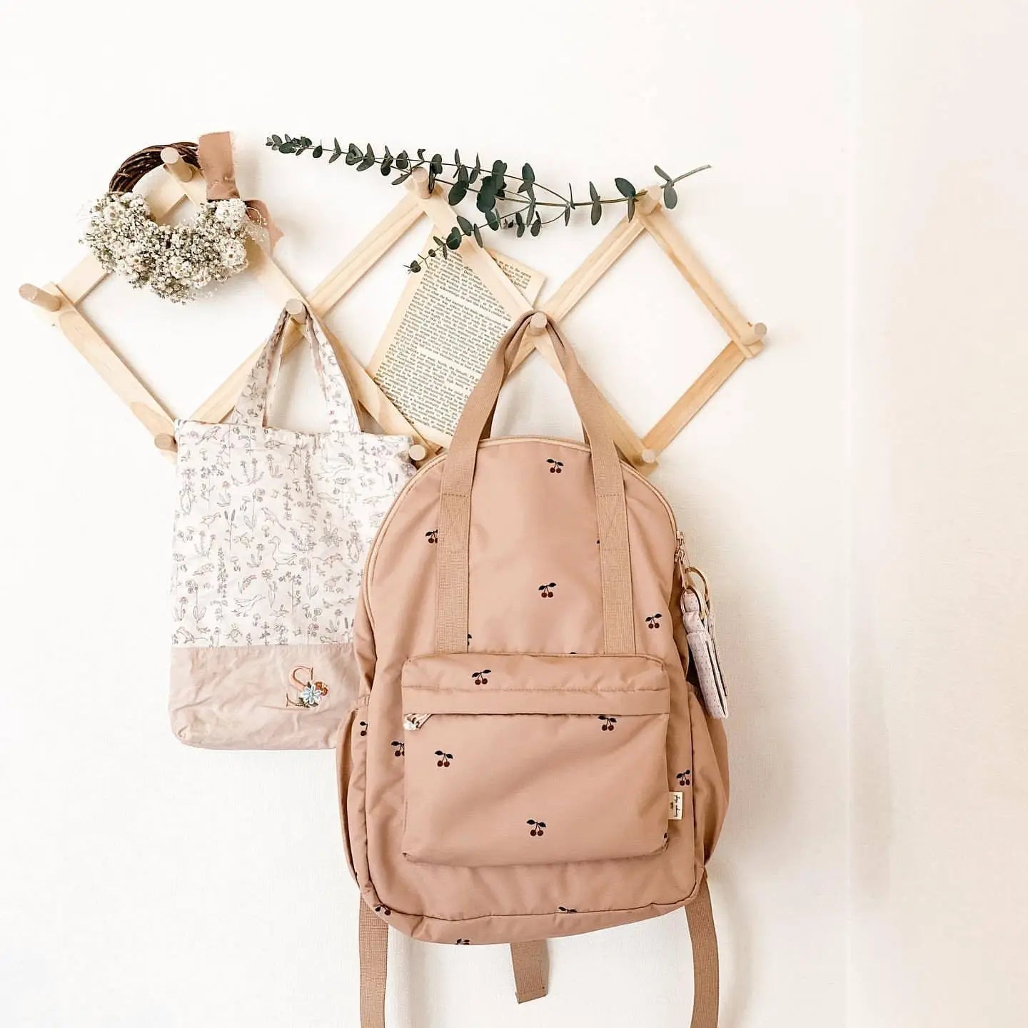 Beiger Kinder-gesteppten, bestickten wasserfesten Schulrucksack mit kleinen schwarzen Beerenmotiven und einer vorne an einem Holzgestell hängenden Vordertasche.