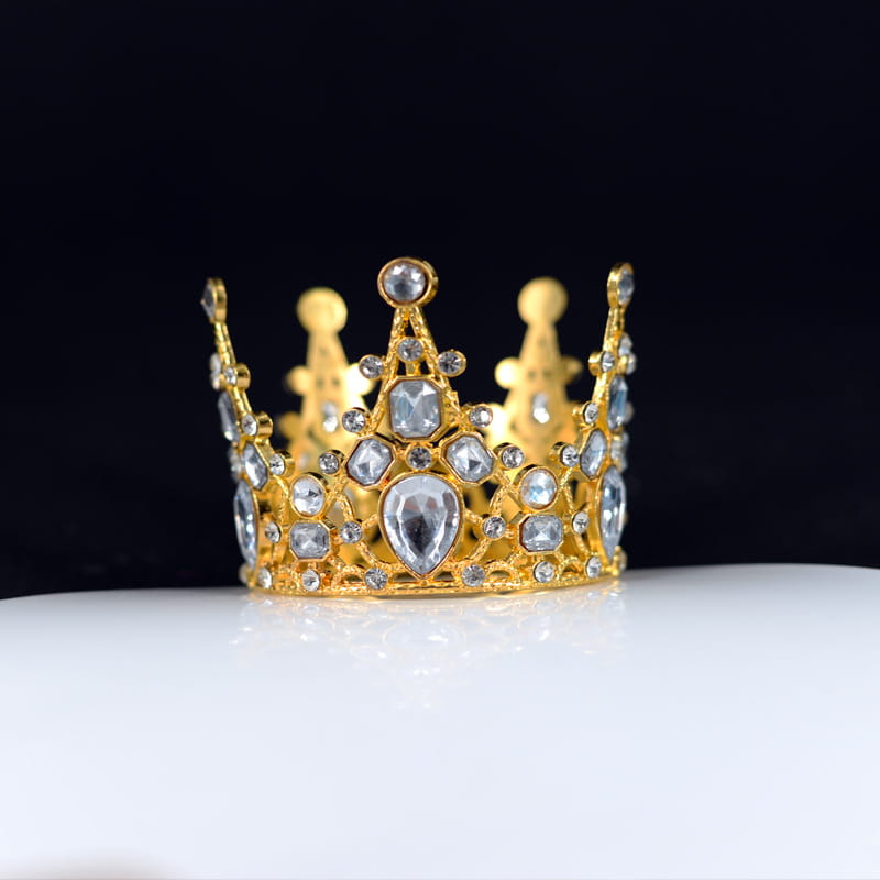 Ein goldener Mini-Kronen-Tortenaufsatz und eine Haar-Tiara, verziert mit klaren facettierten Edelsteinen in unterschiedlichen Größen und Formen.