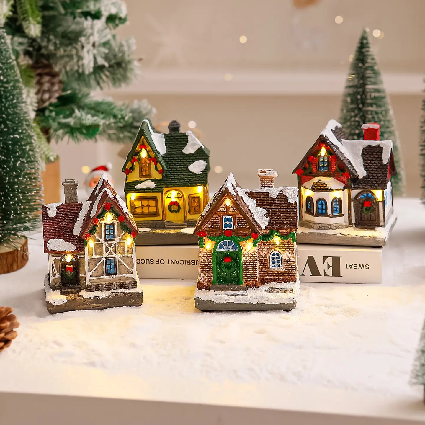 Trois maisons de village de Noël miniatures éclairées avec des toits couverts de neige et des fenêtres lumineuses, en résine ou en plastique peint, ornement pour la décoration des fêtes