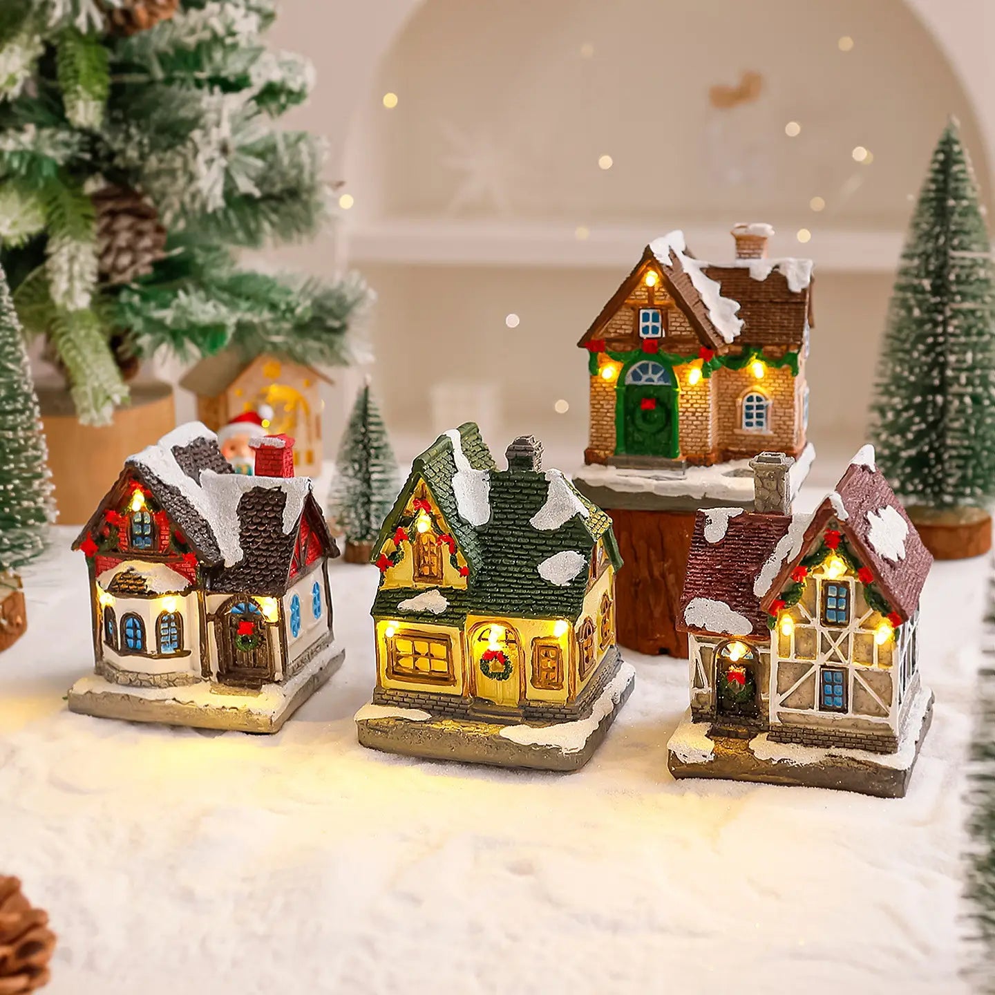 Trois ornements de maison de village de Noël miniature éclairée avec des toits couverts de neige, des décorations festives et des lumières intérieures chaudes.
