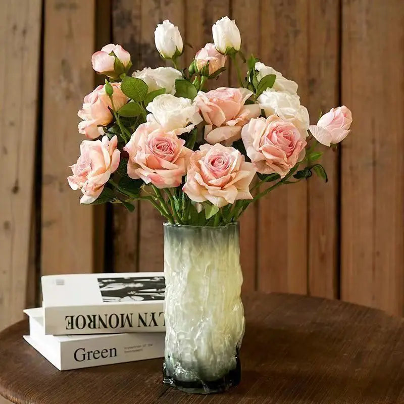 Eine hohe, strukturierte Glassvase mit einem Farbverlauf von hellem Grün bis zu dunklem Grün am Sockel hält in frontaler Ansicht einen Strauß aus rosa- und weißen verwelkten Stielrand-Rosen.