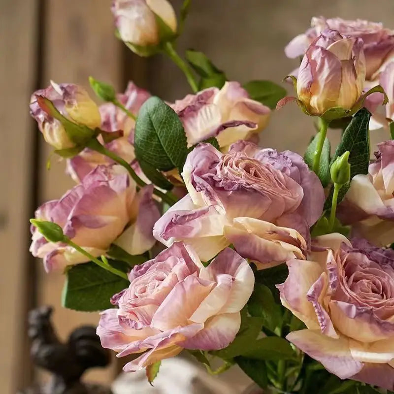 Ein Strauß aus verwelkten Stielrand-Rosen mit zarten rosa- und cremefarbenen Blütenblättern, grünen Stielen und Blättern, von vorne präsentiert.