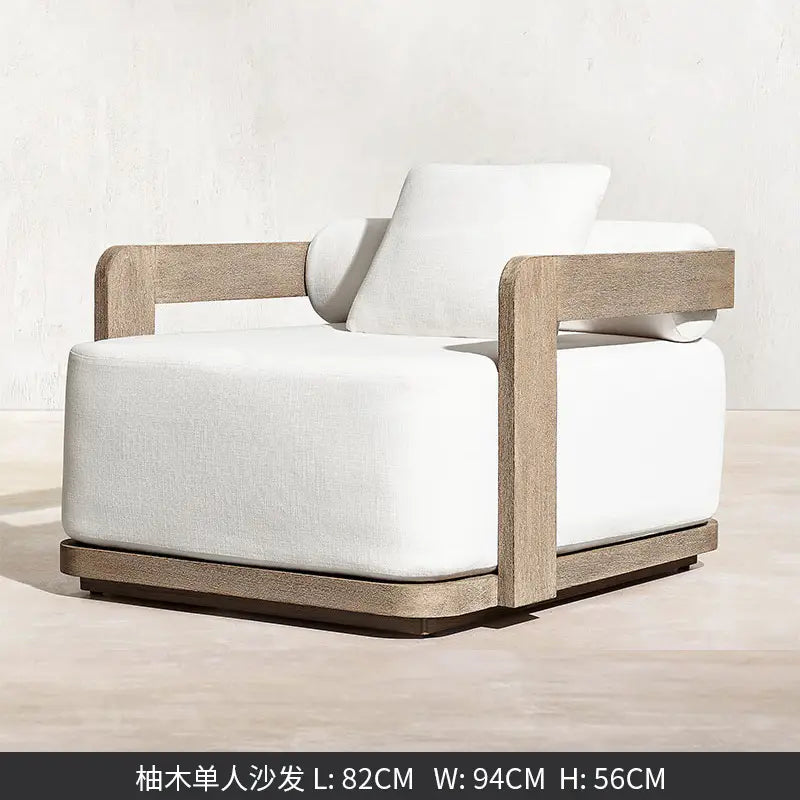 Un fauteuil moderne au style minimaliste, avec un cadre en bois gris clair et un rembourrage en tissu blanc moelleux, provenant d’un ensemble de salon d’extérieur en teck avec section modulaire et brasero.