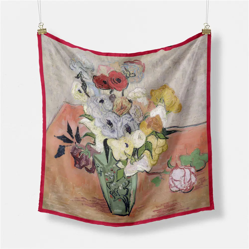 Un foulard carré en soie à bordure rouge éclatante, présentant une peinture florale impressionniste d’un vase vert rempli de roses, de lys et de pivoines, sur une surface aux tons chauds.