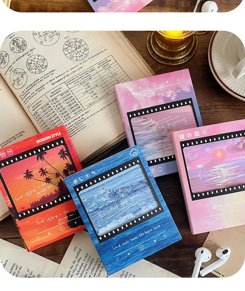 Ensemble de quatre carnets rectangulaires au style ruban de film, avec des couvertures aux couleurs pastel, présentant des scènes de coucher de soleil et d’océan, dans un design de carte de vœux musicale à cassette ruban de film vintage.