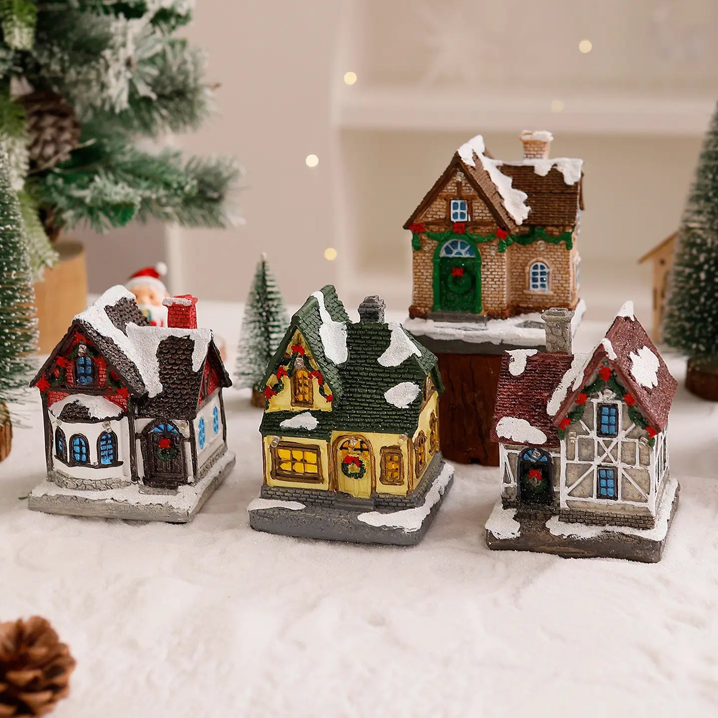 Trois ornements de maison de village de Noël miniature éclairée avec des toits couverts de neige, des décorations festives et des fenêtres illuminées.