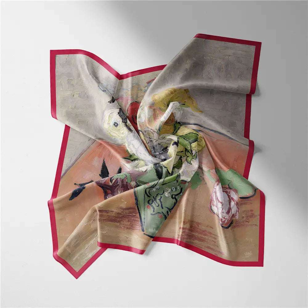 Un foulard carré en soie à motif floral délicatement drapé, avec un design pictural vibrant dans des tons pastel doux et une bordure rouge marquée.