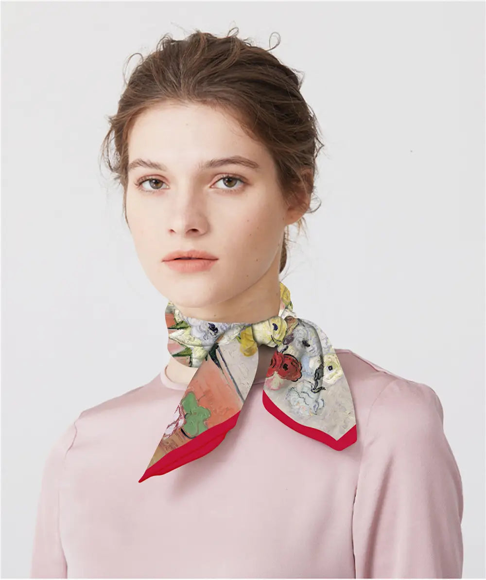 Un foulard carré en soie à motif floral délicat avec une bordure rouge éclatante, noué élégamment autour du cou.