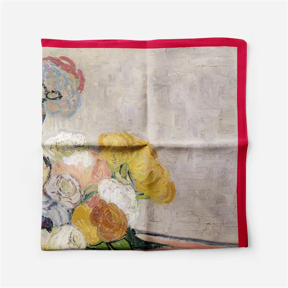 Un foulard carré en soie à bordure rouge à motif floral, présentant une impression de nature morte vibrante avec des fleurs rouges, jaunes et blanches marquées sur un fond gris texturé, encadré par une bordure magenta.