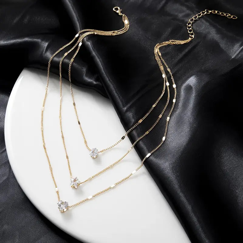 Gold-toned zircon layered pendant necklace for women featuring three delicate chains each with a clear crystal pendant in varying shapes.