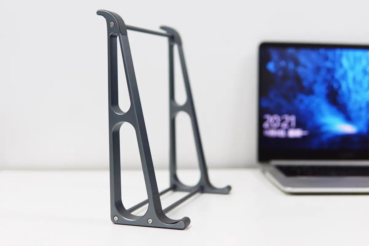 Dark gray metal Orico portable aluminum laptop stand with sleek minimalist design featuring cut-out oval shapes and sturdy legs for desktop riser use.