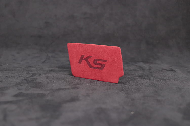 Kia K5 スエードカーボン インテリア ドアハンドルカバーとして設計された、エンボス加工のksロゴ入りの赤いスエード風長方形カードホルダー。
