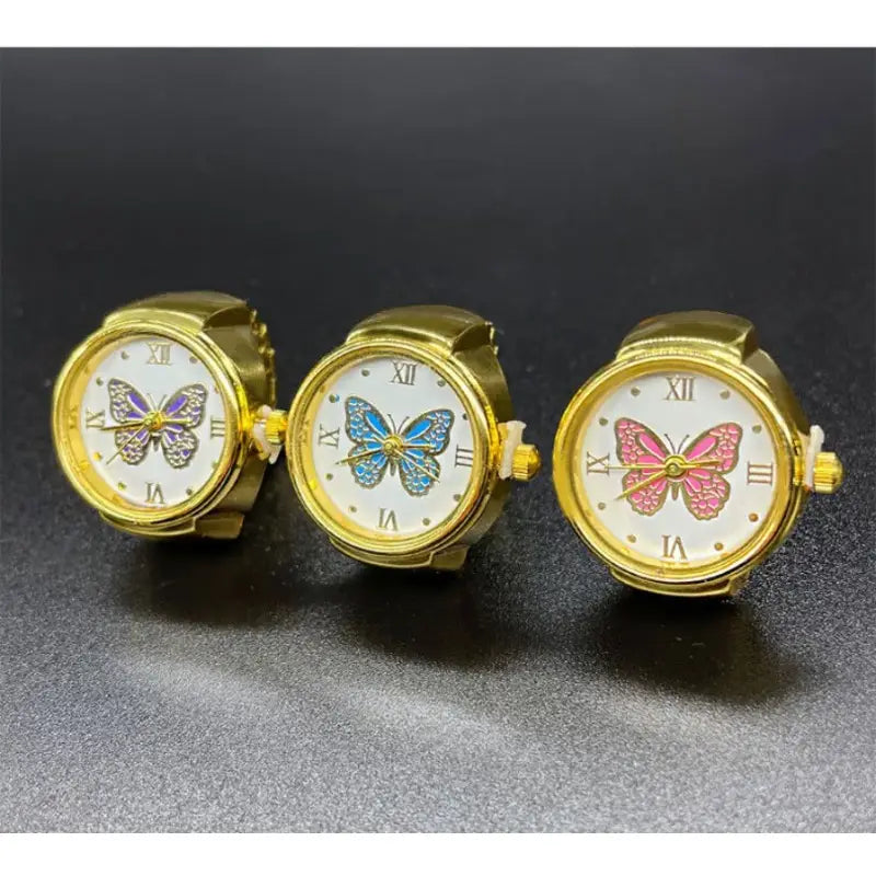 Three gold-toned stainless steel butterfly-themed wristwatches with white faces, roman numerals, and uniquely colored enamel butterfly designs in a cute jewelry collection.