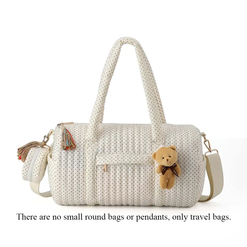 Eine cremefarbene gepolsterte Kinderwagen-Organizer-Tasche mit schwarzen Pünktchen, mit kuscheligem Teddybär-Anhänger und Akzenten mit Quasten.