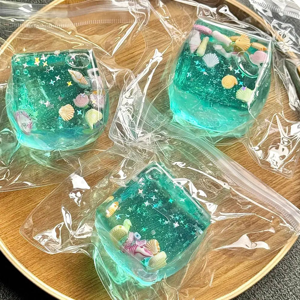 Durchscheinende tealfarbene Seifen aus Harz mit eingearbeiteten Muscheln, sternförmigem Glitzer und Miniatur-Fischfigürchen, von vorn als nachdenkliches Geschenk dargestellt.