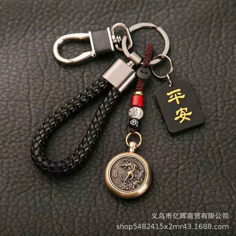 赤と銀のビーズでアクセントを施し、刻印された「龍」のデザインをあしらったブロンズ円形ペンダントと、金色の漢字が記された黒いタグを備えた黒の編みレザー製キーチェーン（中国の干支をモチーフにした編みレザー製ラッキーペンダント）。