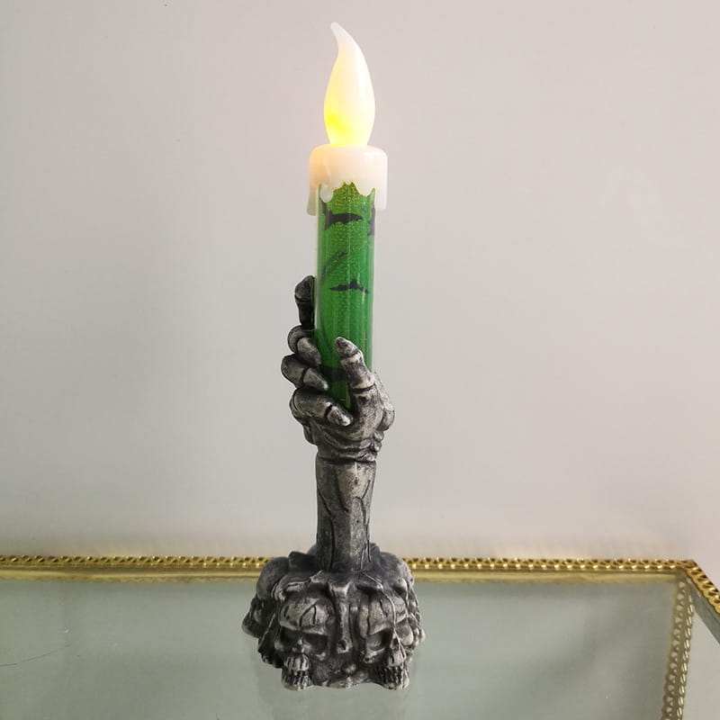 a green led candle with a glowing flame held by a silver skeleton hand and a skull-adorned base designed for a happy halloween party and party happy halloween events