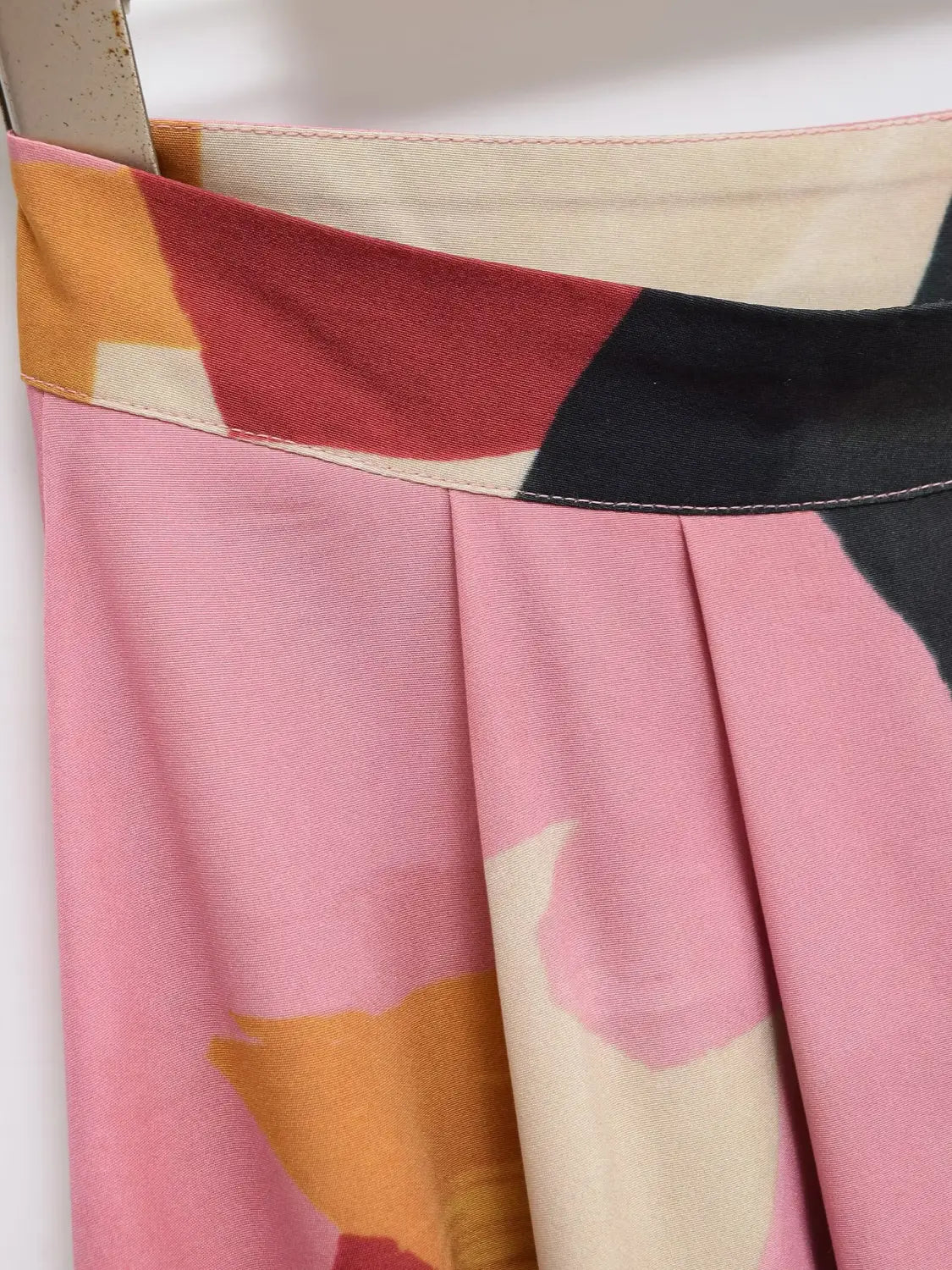Ein plissierter rosa Satin-Midirock mit einem kräftigen geometrischen Muster in Tönen von Rot, Schwarz und Orange.