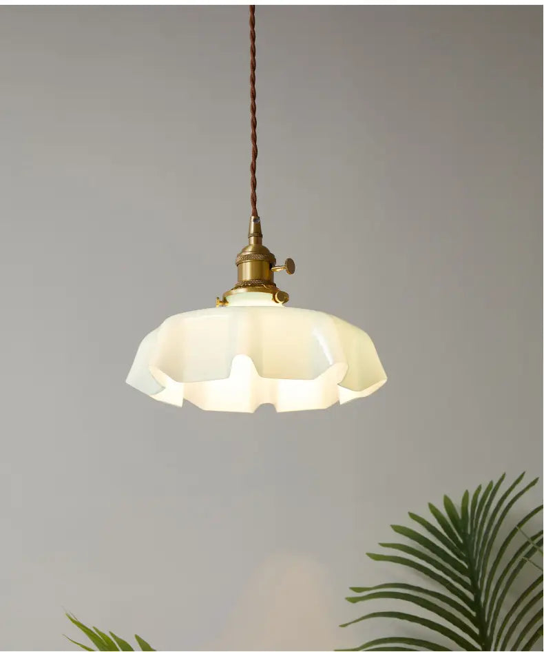 Un luminaire suspendu de style vintage avec un abat-jour à jupe florale en verre cannelé de couleur crème et une tête de lampe en cuivre suspendue par un cordon brun torsadé.