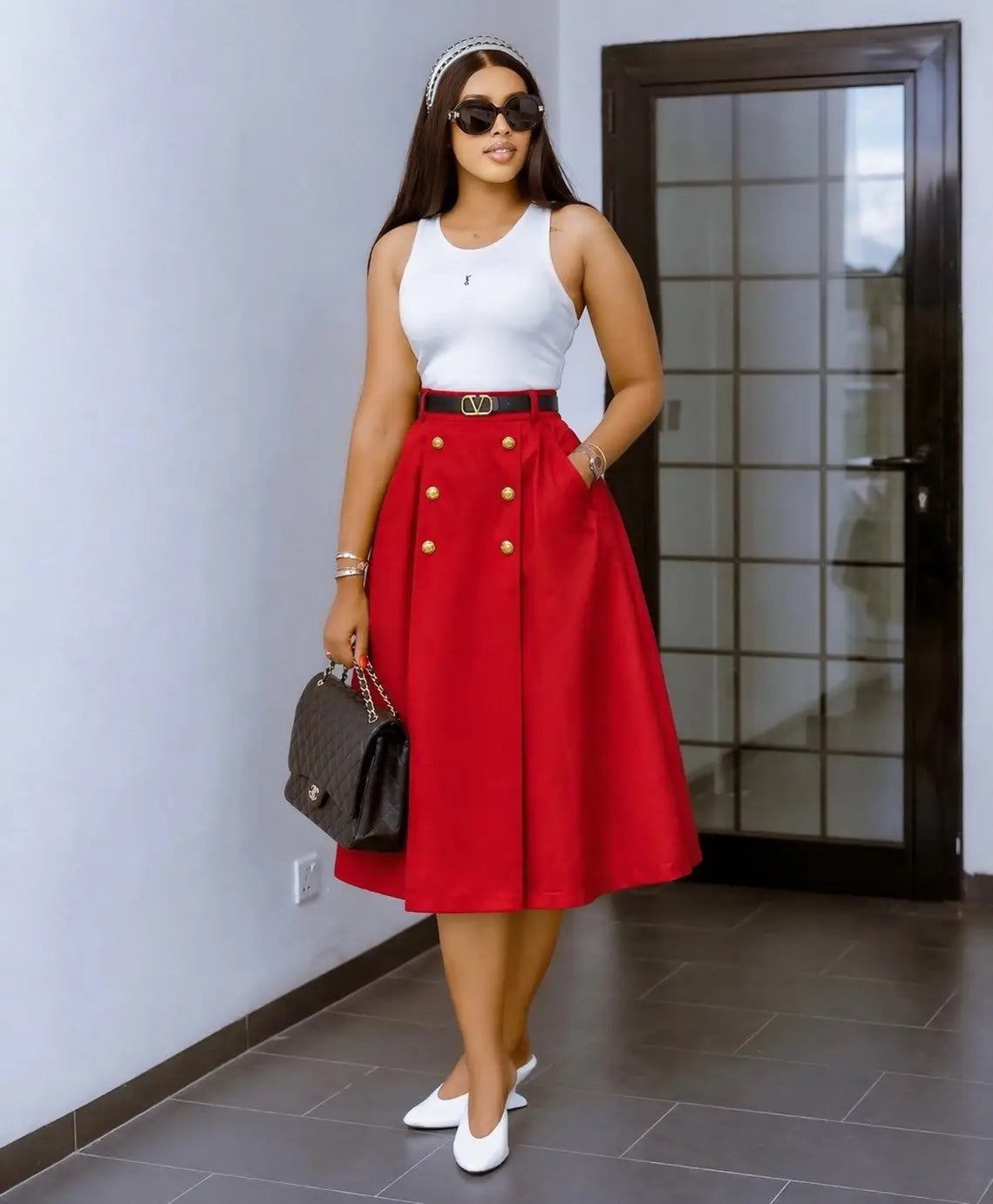 Jupe midi en maille à taille haute rouge, à double boutonnage avec des boutons dorés et une ceinture noire munie d’une boucle en forme de V.