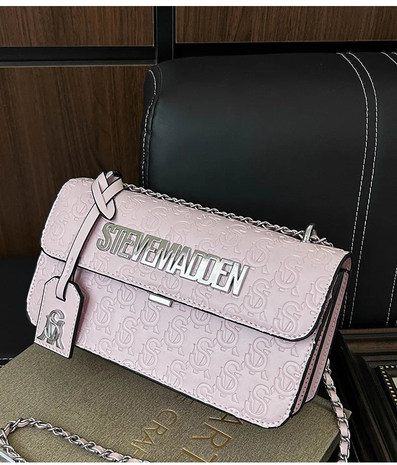 Eine hellrosa Steve Madden gesteppte Umhängetasche mit dezenter Relief-Logo-Musterprägung, Metallbranding in Silberoptik und Kettentrageriemen.