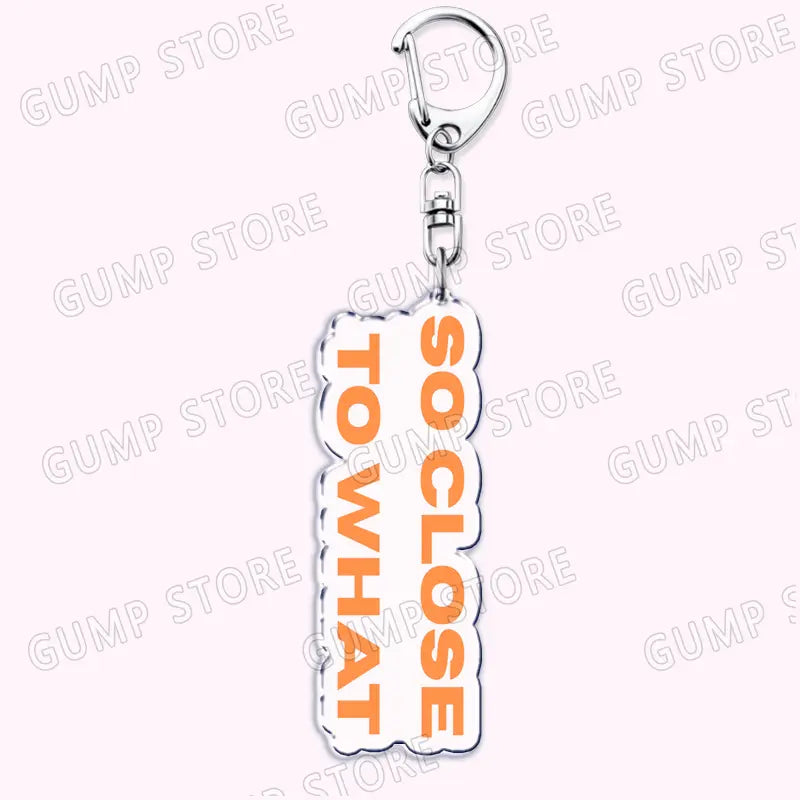 a white acrylic keychain with orange text reading so close to what and a silver metal clasp designed as a music fan gift tate mcrae acrylic keychain