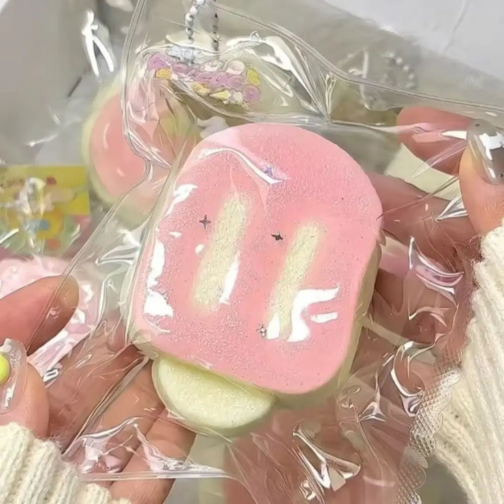 Un jouet antistress « squeeze » rose et blanc qui remonte lentement, avec un mignon design de visage, maintenu dans un emballage en plastique transparent pour soulager le stress sensoriel.