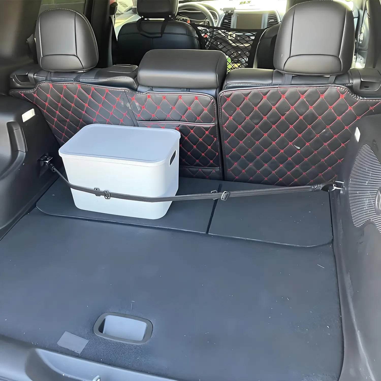 white plastic storage box with gray lid secured by black elastic straps across the back of a car trunk as a trunk organizer.